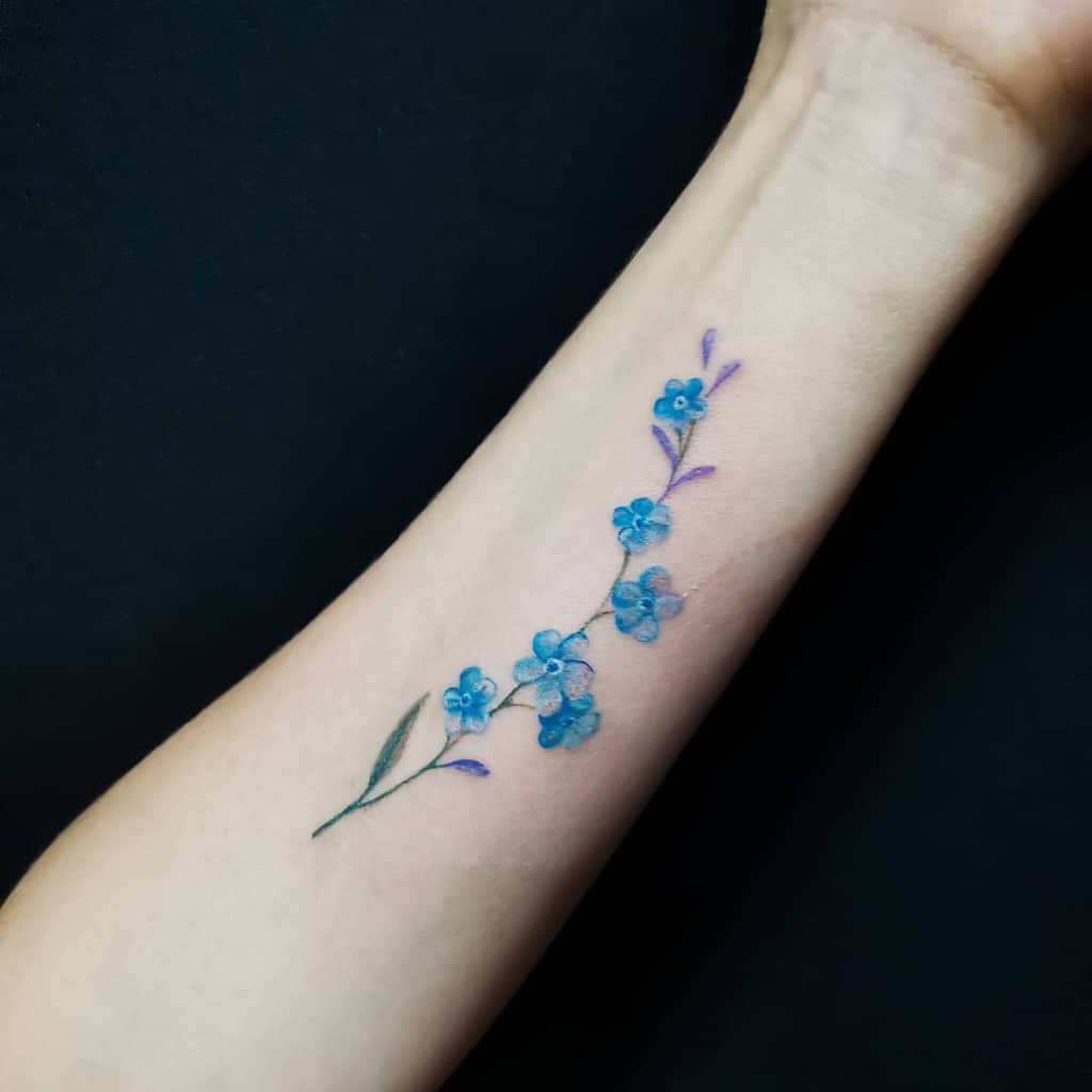 A delicate blue floral tattoo of forget-me-nots rests gracefully on a forearm