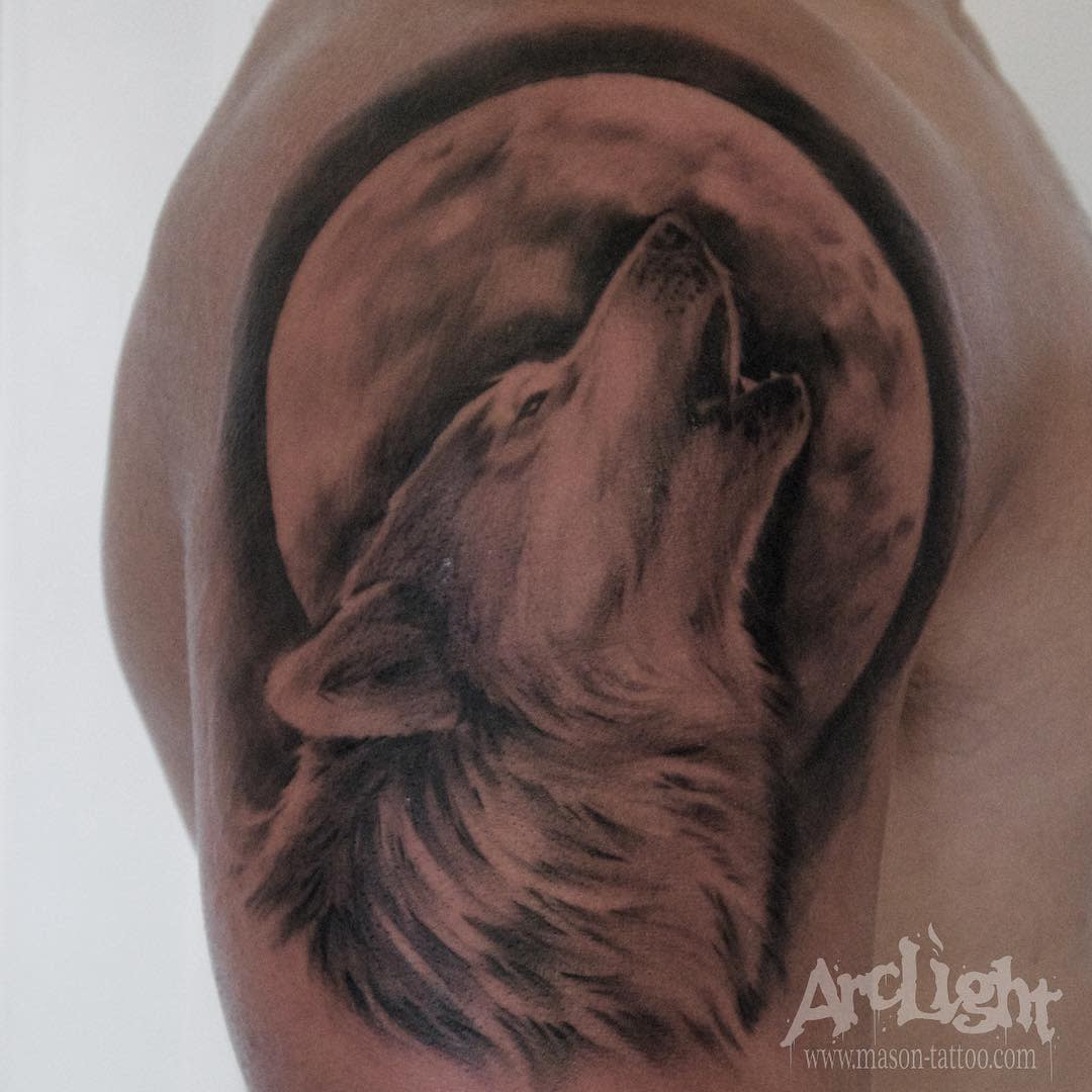 Tattoo of a wolf howling at a full moon on an upper arm