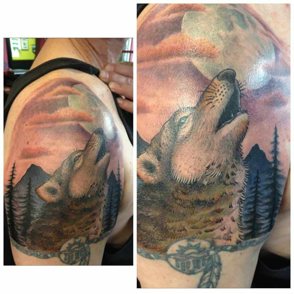 A wolf tattoo on an arm, howling at the moon with trees and a feather in the design