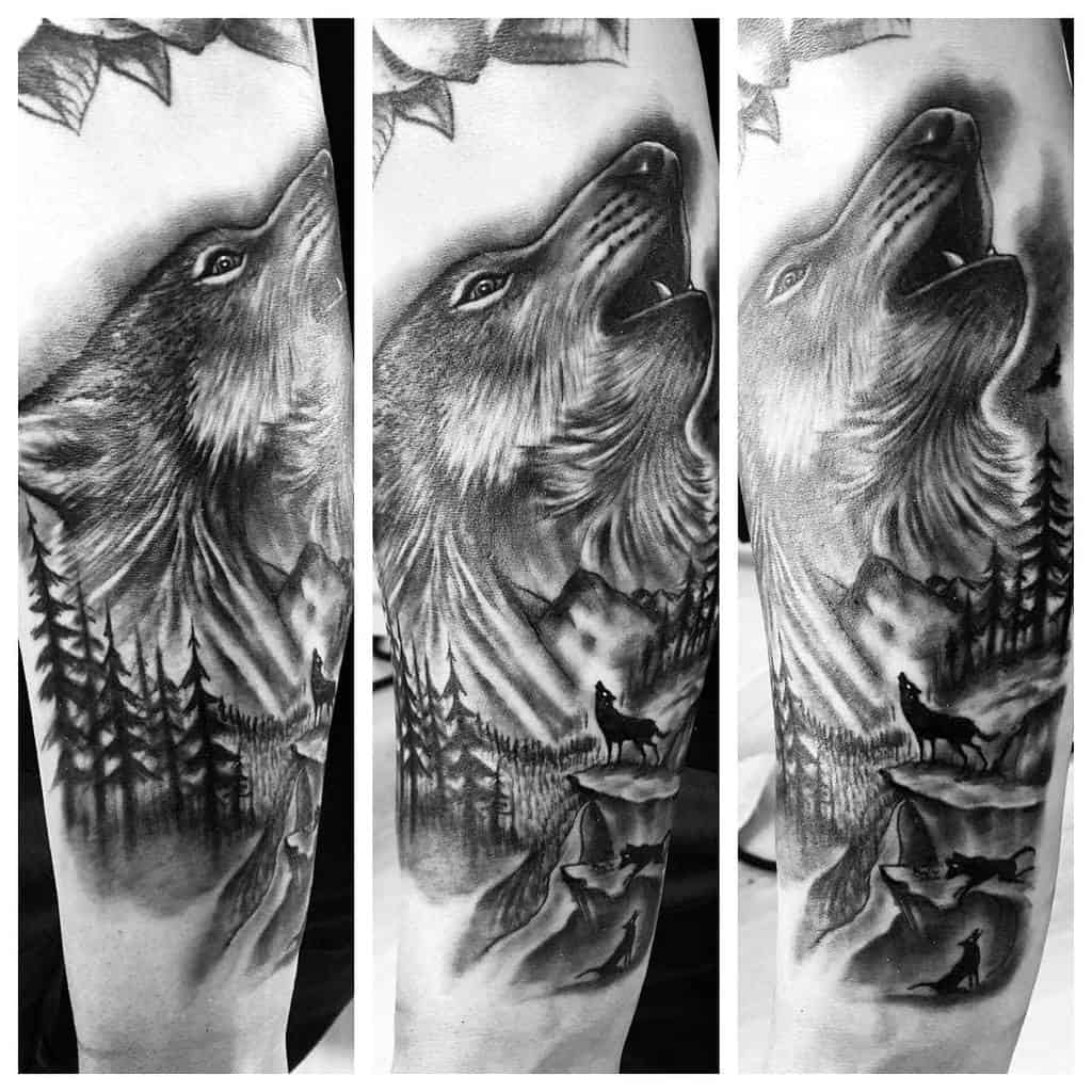 Black and white tattoo of a howling wolf with trees and mountains in the background