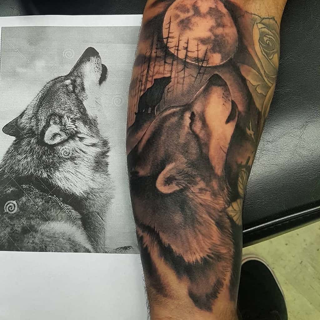 Realistic forearm tattoo of a howling wolf beneath a full moon, surrounded by trees and shadowed rose details