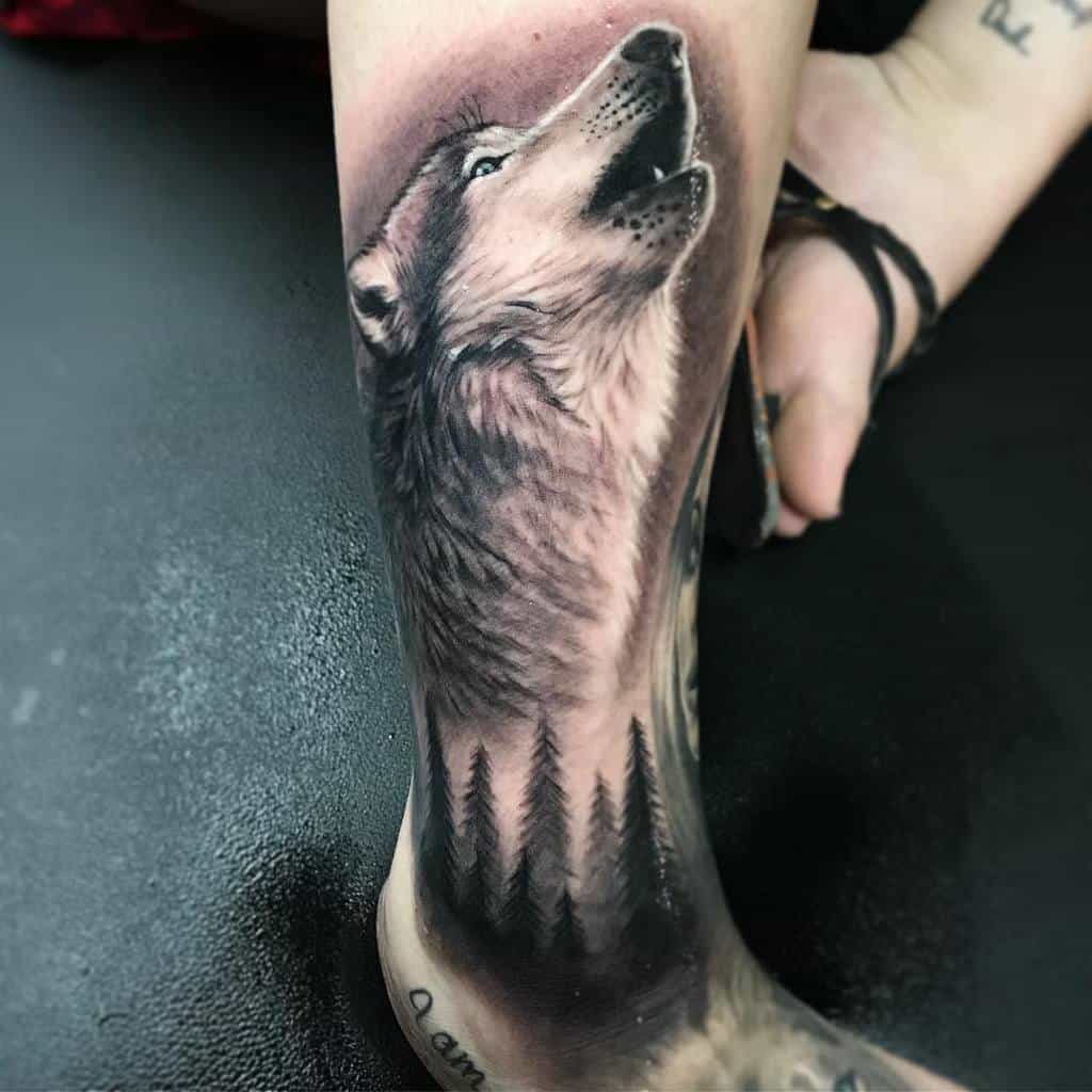 Tattoo of a howling wolf and trees on a lower leg