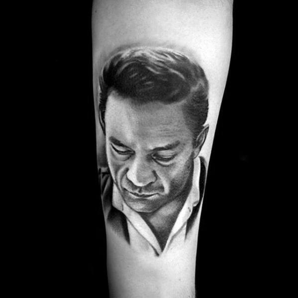 Tattoo of Johnny Cash looking down on a person's arm in black and gray tones