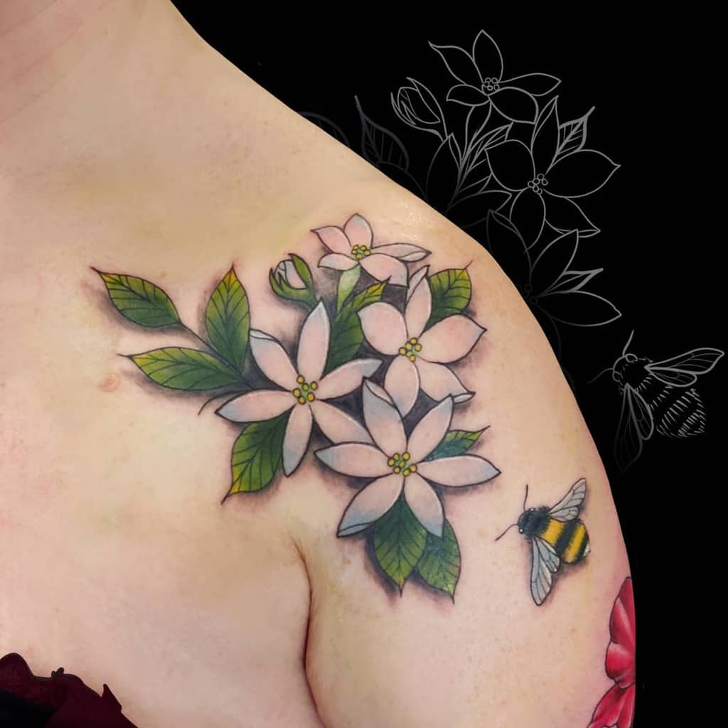 A tattoo of white jasmine flowers and leaves with a bee on a shoulder