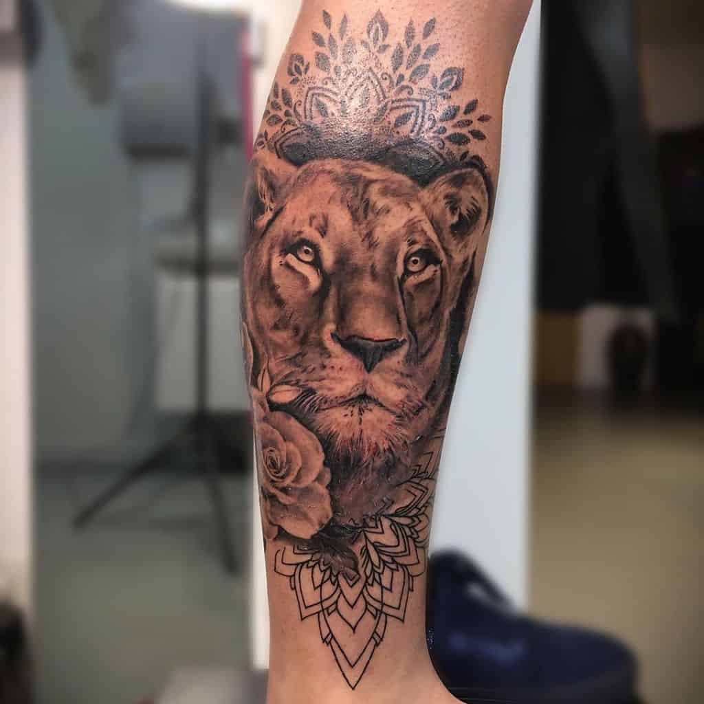 Realistic lioness tattoo on the forearm, featuring intricate shading, floral and mandala elements, blending power and elegance in a bold design.