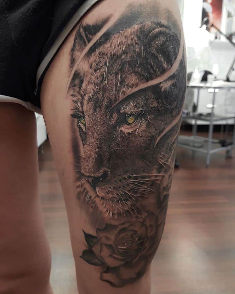 Hyper-realistic lioness tattoo on the thigh, featuring lifelike fur details, piercing green eyes, and a rose for a bold yet elegant design.