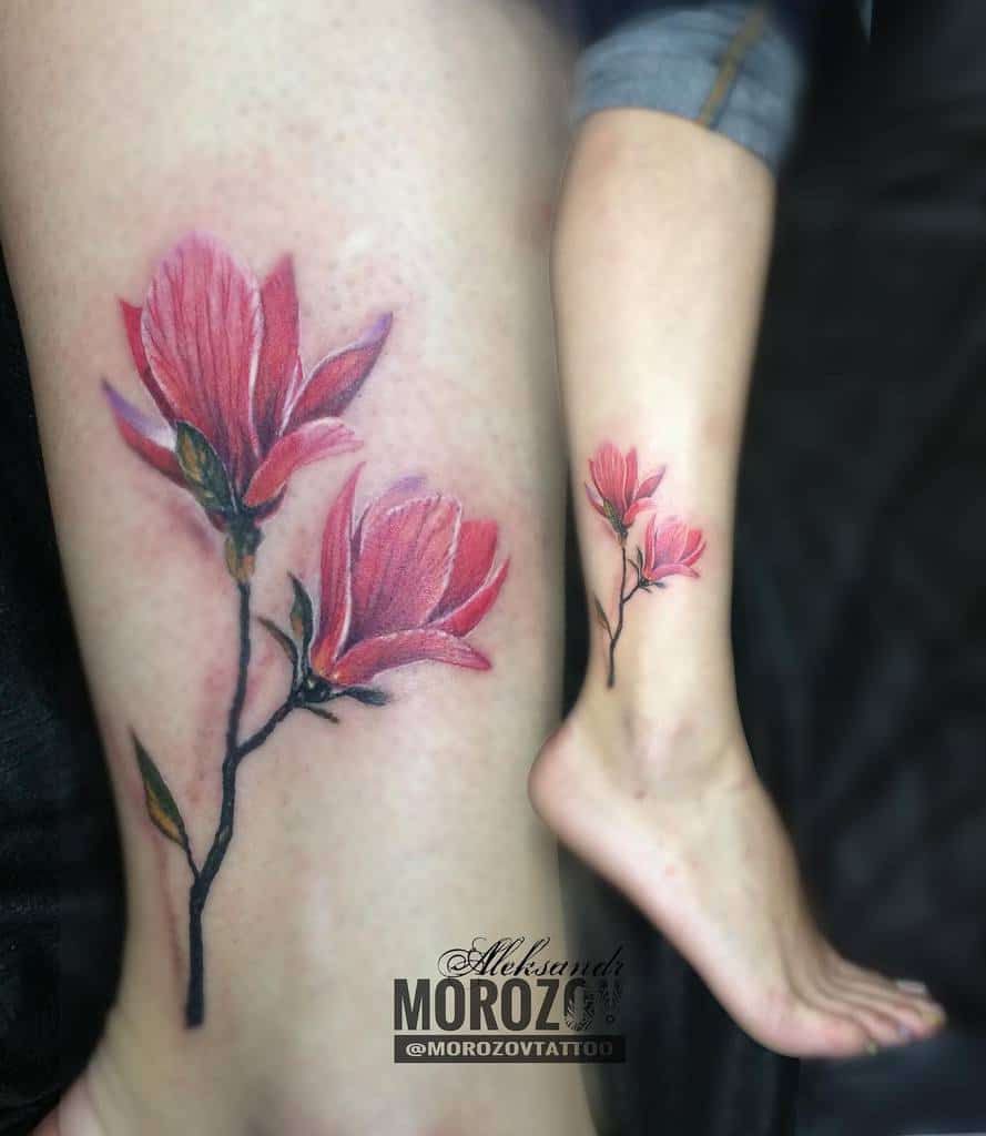 A leg adorned with a detailed magnolia tattoo, showcasing pink flower petals and vibrant green stems in stunning realism