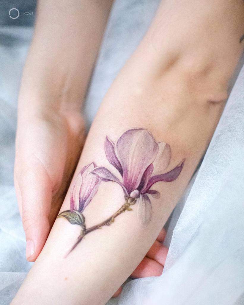 A lifelike magnolia flower tattoo graces the forearm, capturing nature's elegance