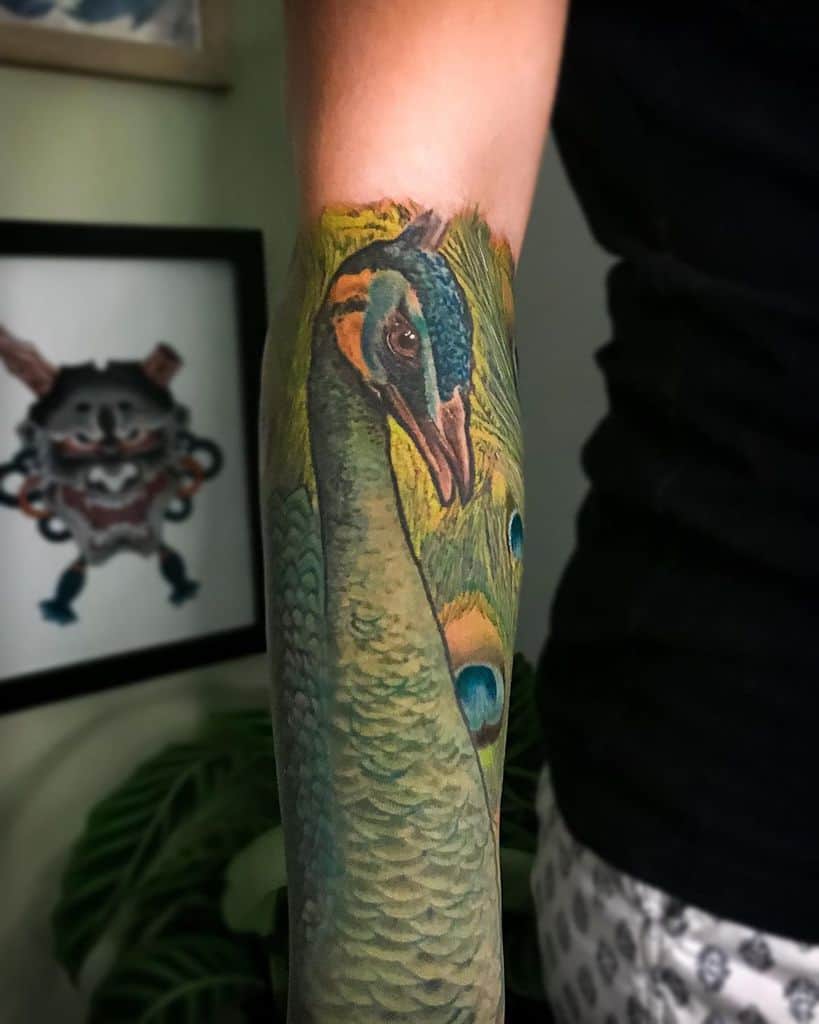 Vibrant and detailed peacock tattoo covering the forearm, showcasing the bird’s vivid feathers and naturalistic design.