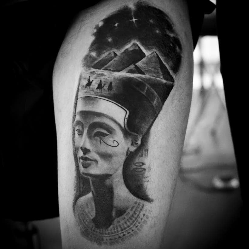 Black and white tattoo of Queen Nefertiti with pyramids and a night sky on an arm
