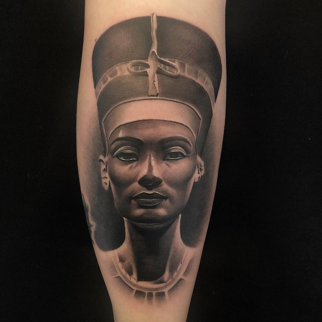 Black and gray tattoo of Queen Nefertiti on forearm against a dark background