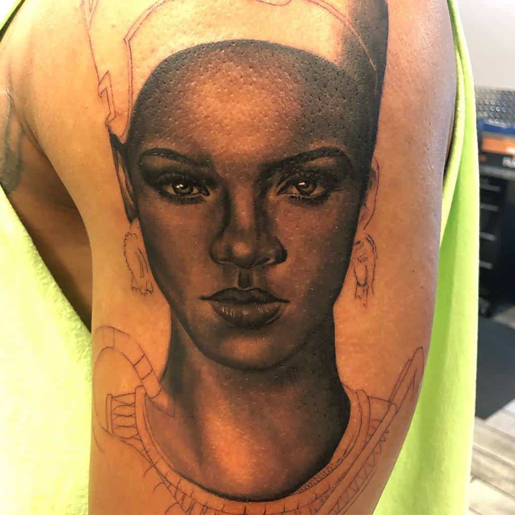 Tattoo of Rihanna with a headdress and earrings on an arm
