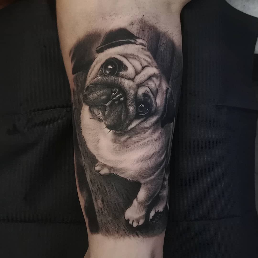 A highly detailed black-and-white tattoo of a pug looking up, standing on a wood, set against a softly shaded background