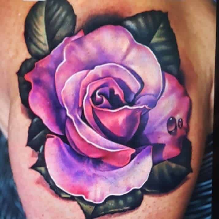 Vibrant purple rose tattoo with green leaves on skin