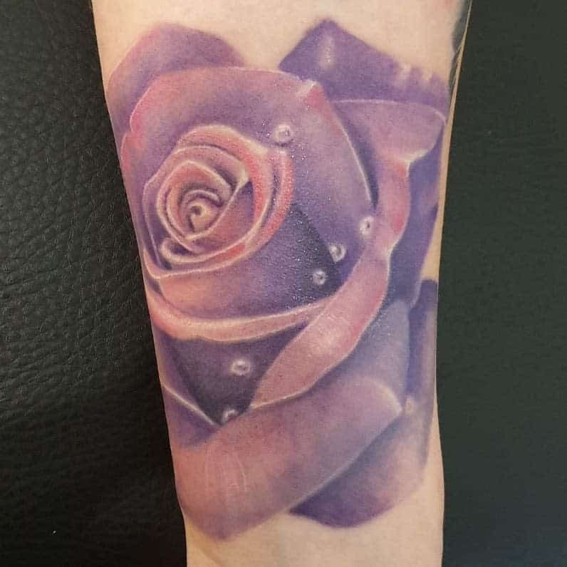 Tattoo of a purple rose with dew drops on forearm