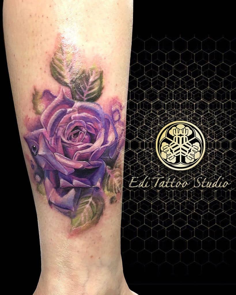 Purple rose tattoo with green leaves on a leg