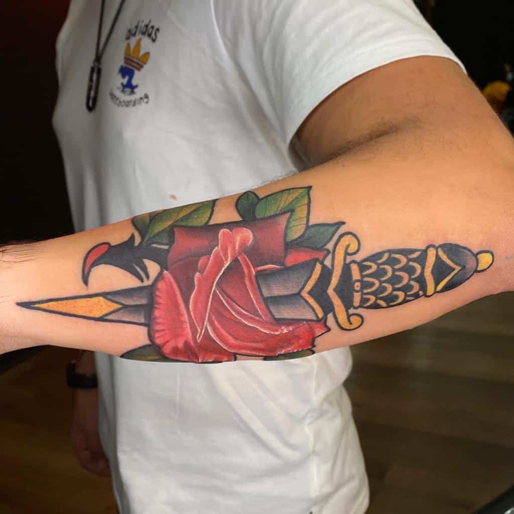 Tattoo of a dagger and red rose on a man's forearm