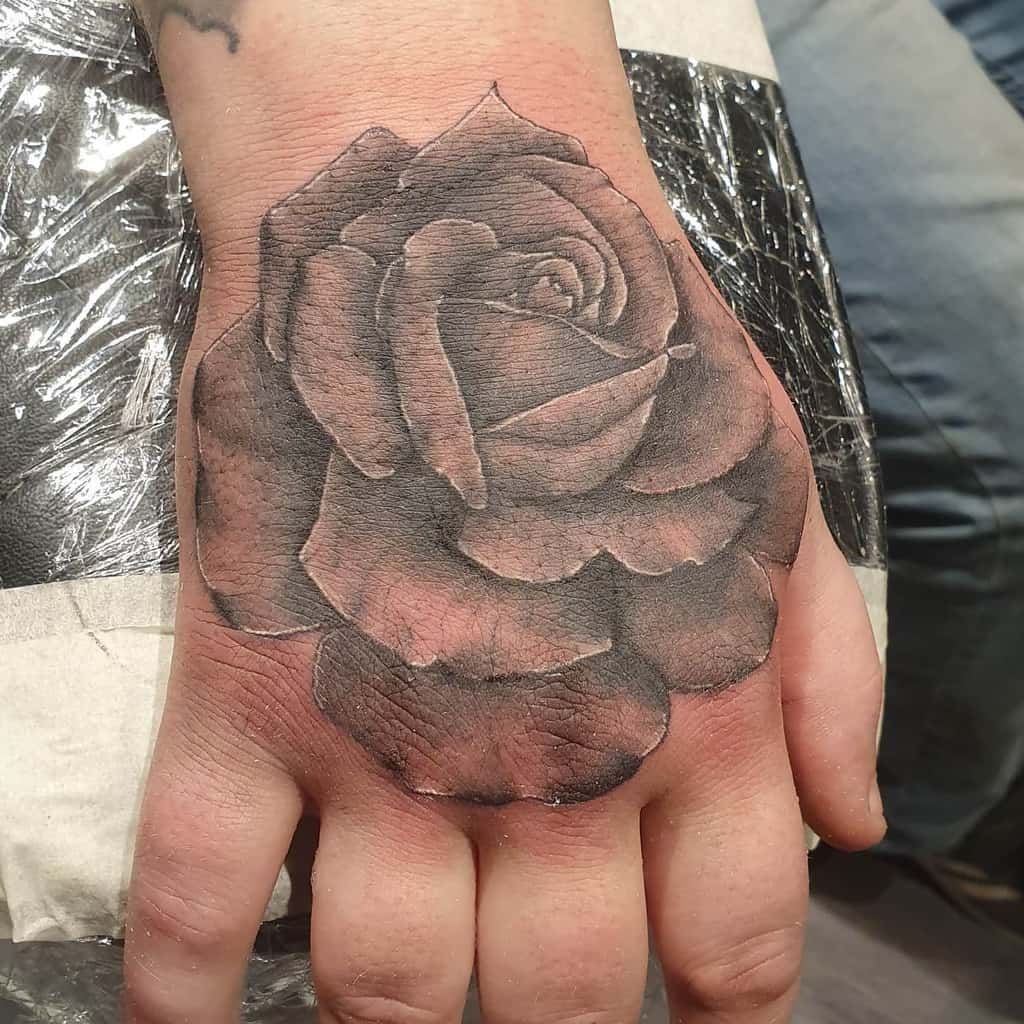 A captivating black rose tattoo graces the back of a hand, showcasing exquisitely detailed petals and subtle shading