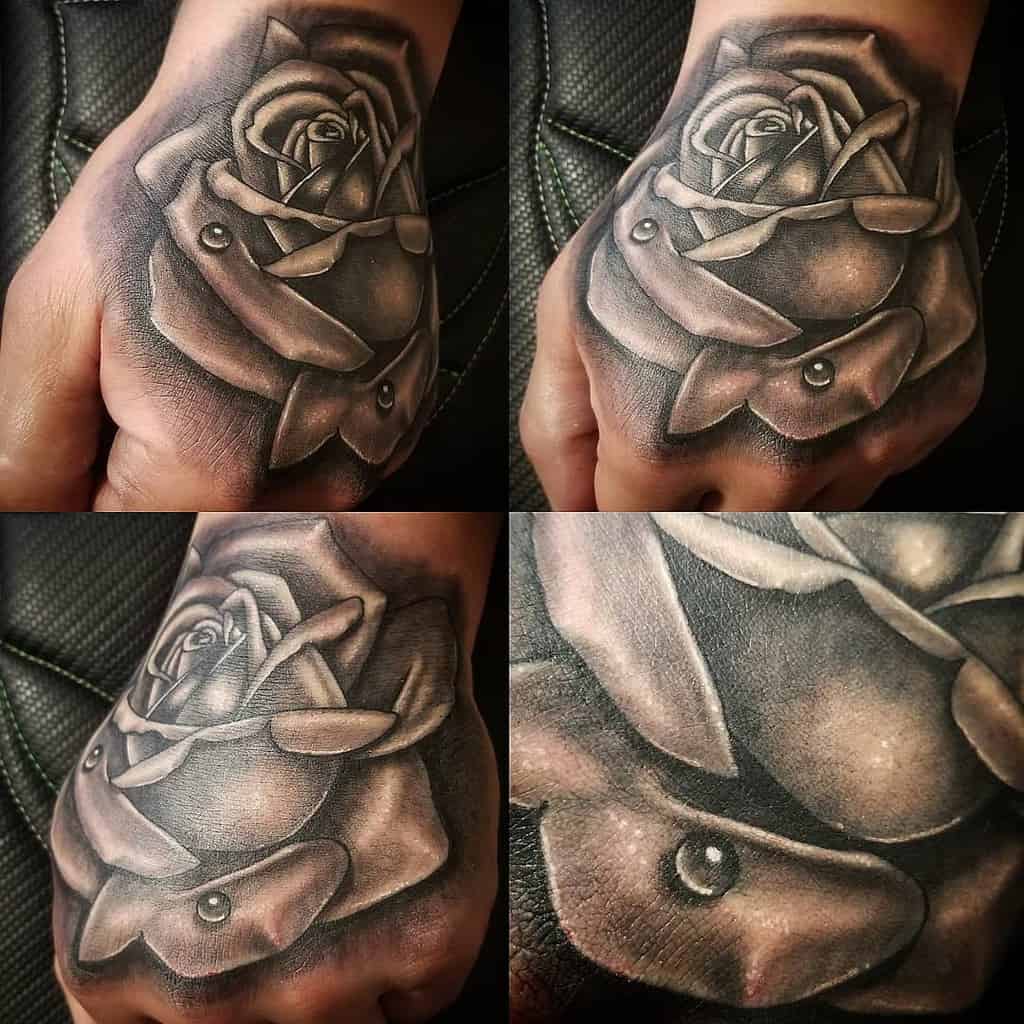 A detailed black and gray realistic rose tattoo on the hand, featuring soft shading and delicate highlights