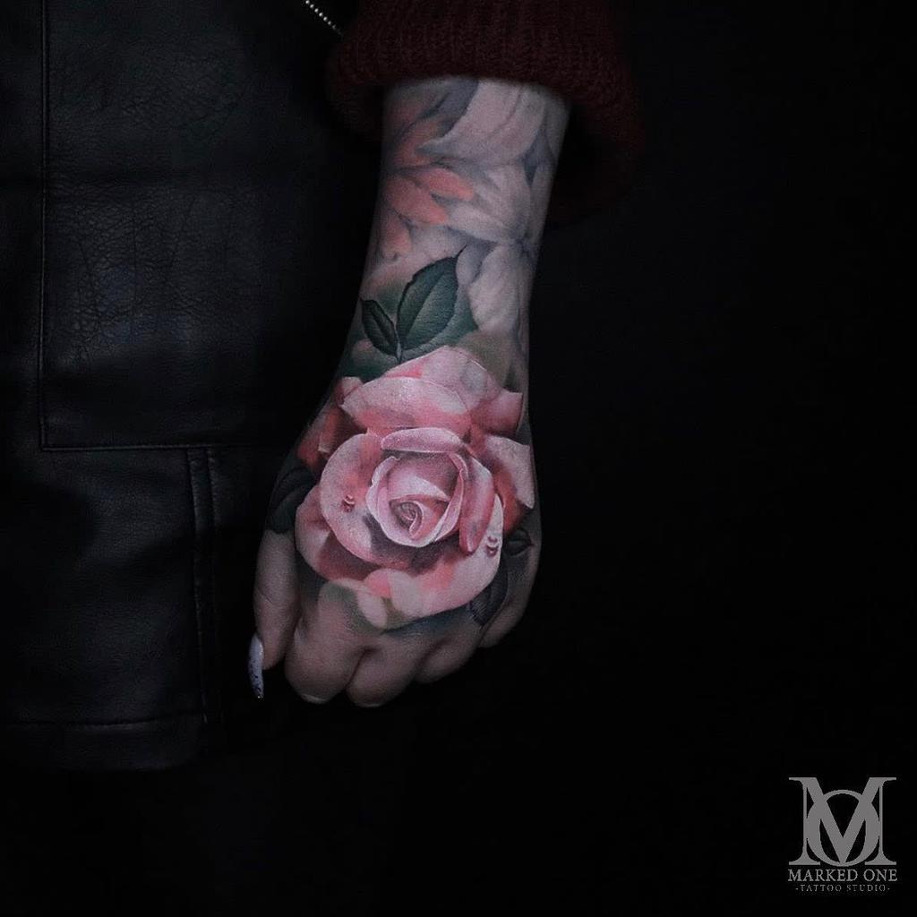 A tattooed hand featuring a stunningly realistic pink rose
