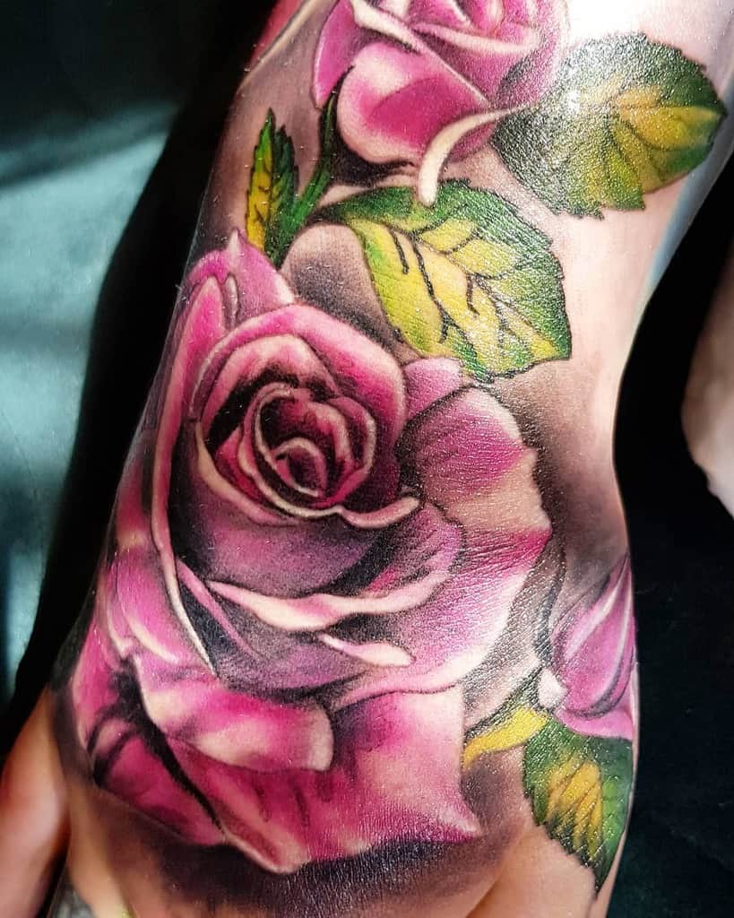 Close-up of a vibrant purple rose tattoo with lush green leaves