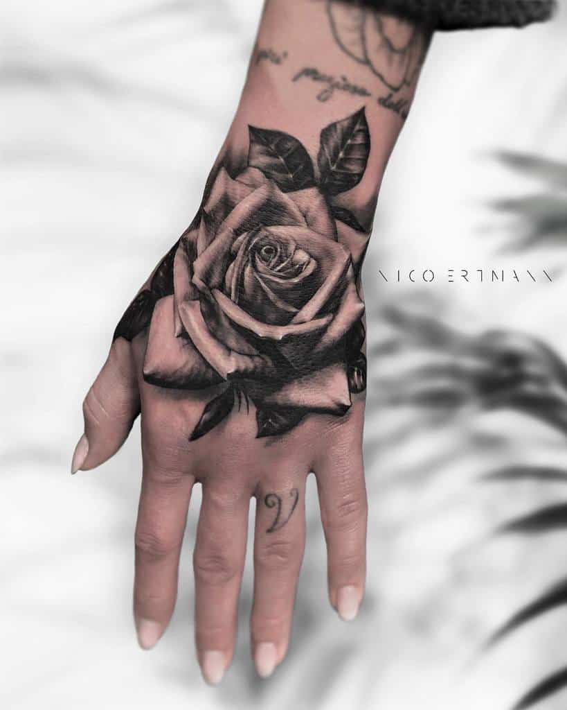 Hand tattoo with a beautifully detailed black and gray rose design elegantly blooming across the back of the hand