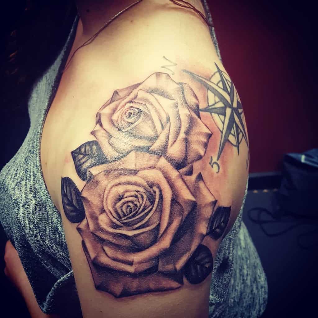 Tattoo of two roses and a compass beautifully adorning the shoulder and upper arm