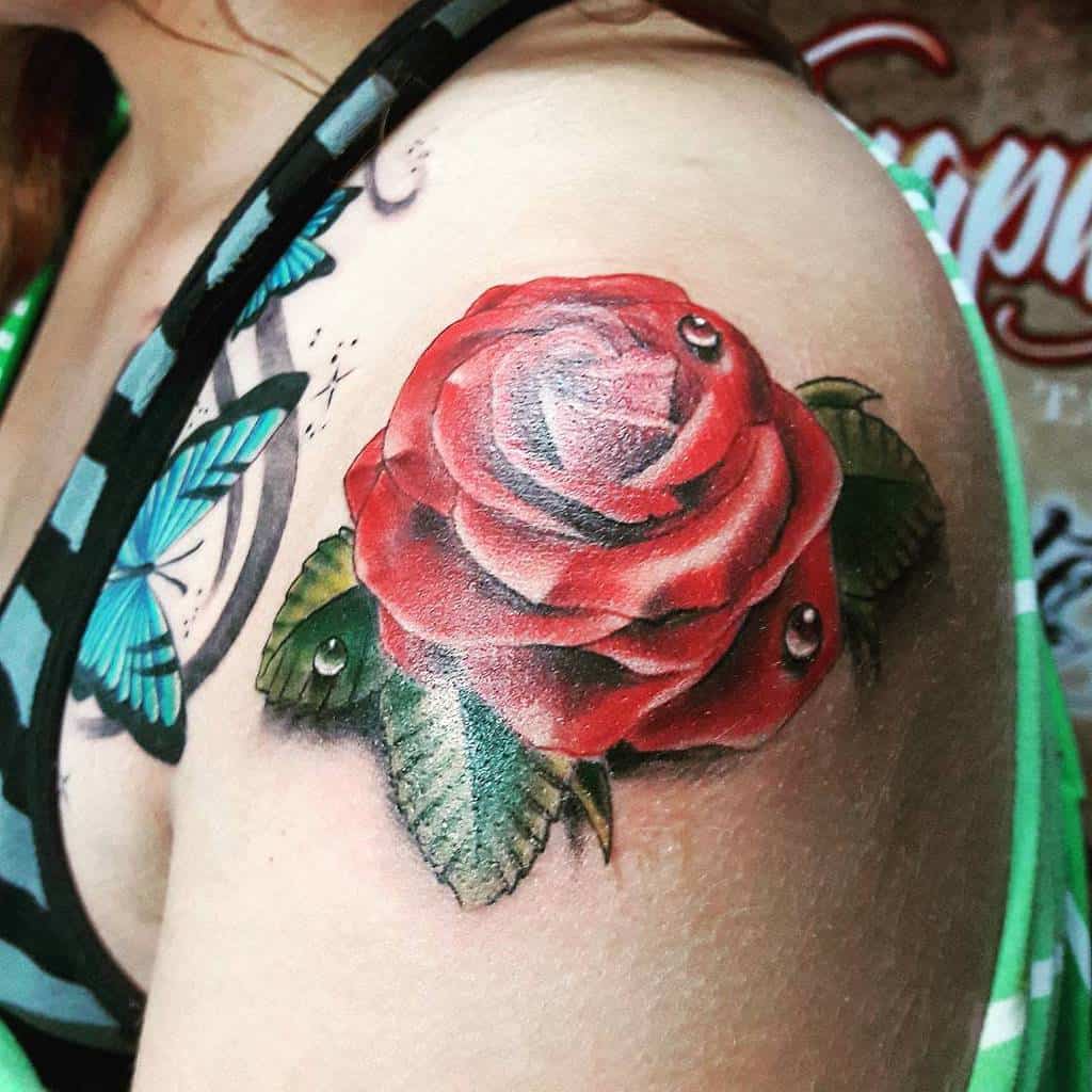 A vibrant red rose tattoo adorned with dewdrops graces a person's shoulder