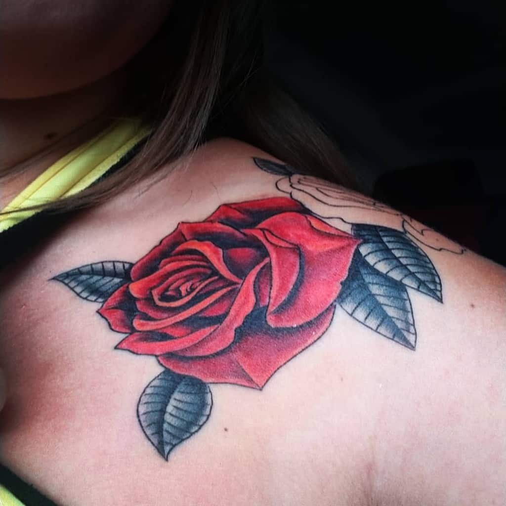 A striking close-up of a red rose tattoo adorns the shoulder, accompanied by vibrant black leaves