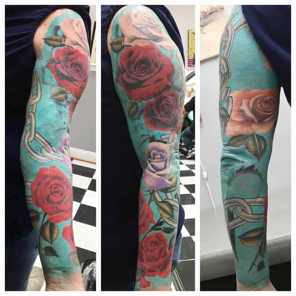 Tattooed arm with roses and chains on a turquoise background