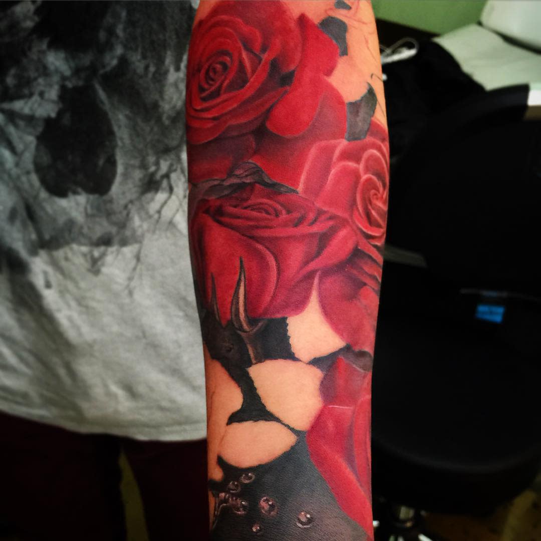 Forearm tattoo sleeve featuring vibrant red roses intertwined with abstract black designs