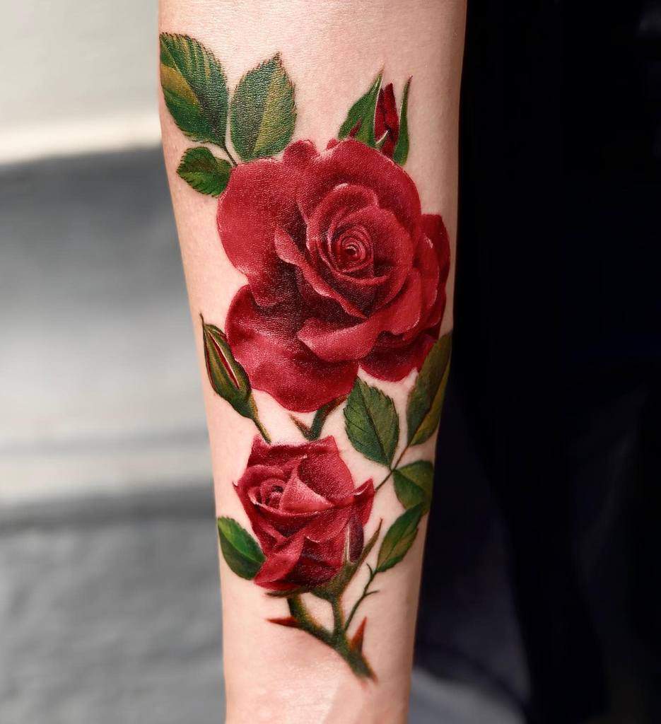 Realistic forearm tattoo showcasing two deep red roses with rich green leaves, creating a lifelike and vibrant floral design