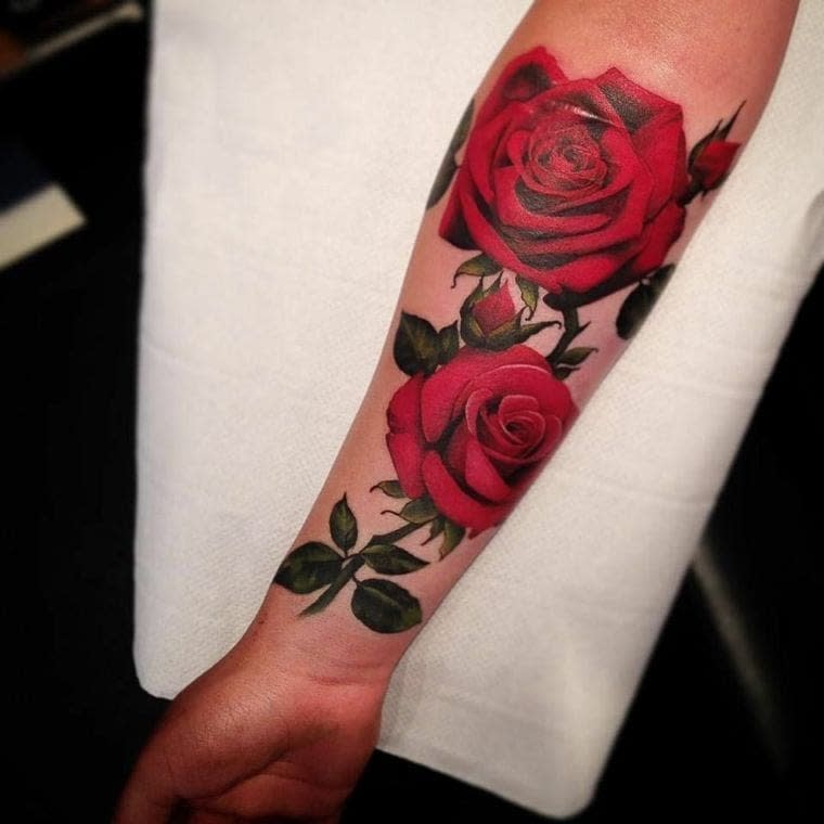 Vivid forearm tattoo featuring two bold red roses with detailed green leaves, creating a striking and lifelike floral design