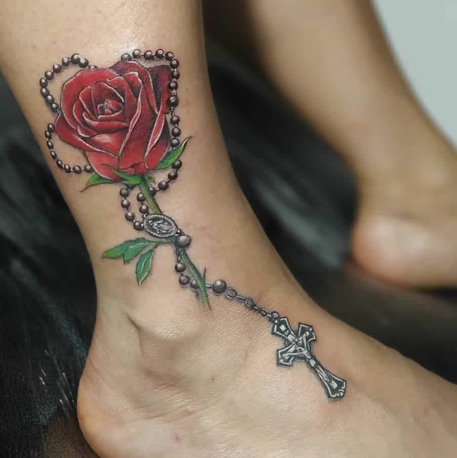A tattoo of a rose, its stem gracefully entwined with a rosary and cross, adorns the ankle