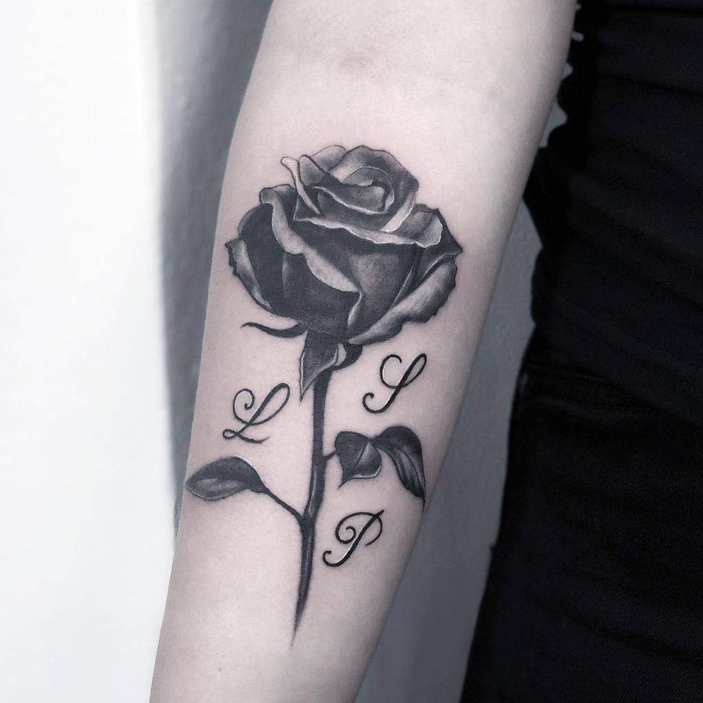 A tattoo of a rose with the letters "L," "S," and "P" gracefully entwined along its stem adorns the arm