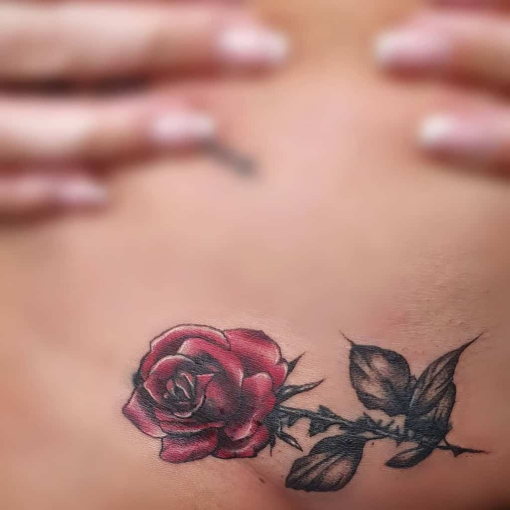 Close-up of a red rose tattoo with green leaves and a slender stem on skin