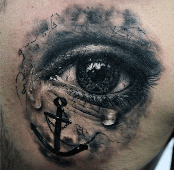 Realistic tattoo of an eye featuring an anchor and teardrops, shaded in grayscale