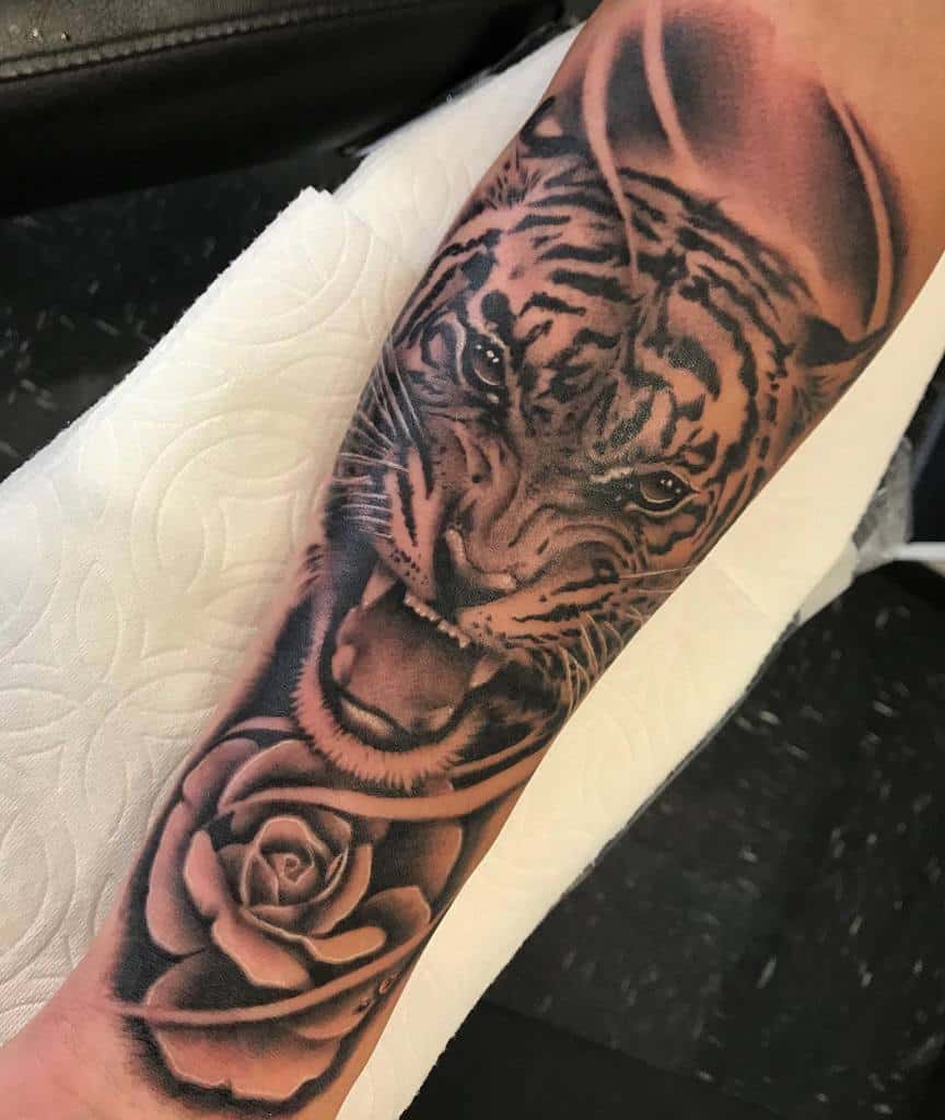 A stunning tattoo featuring a roaring tiger intertwined with a delicate rose adorns the person's forearm