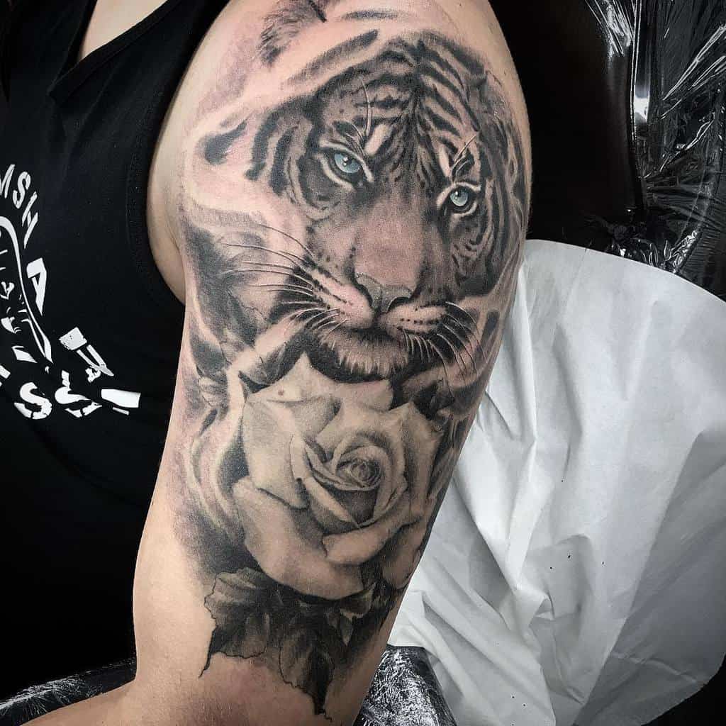 A stunning tattoo on a person's upper arm features a majestic tiger intertwined with a blooming rose, capturing strength and beauty in perfect harmony