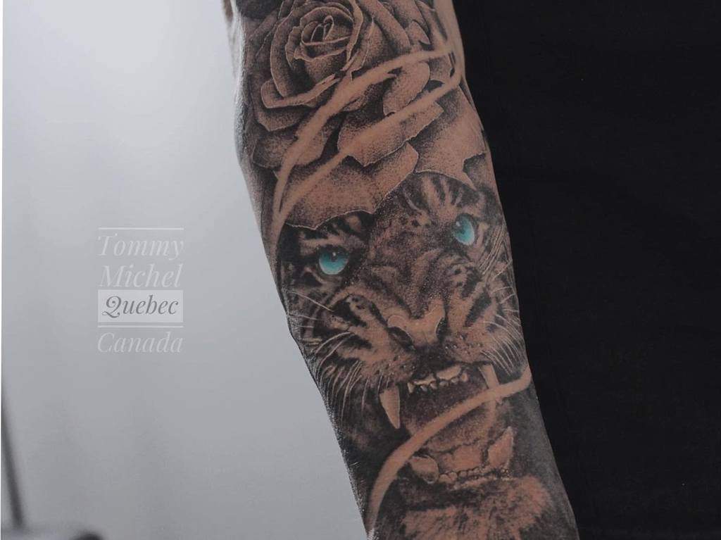 A detailed tattoo of a tiger with blue eyes intertwined with a rose on a forearm