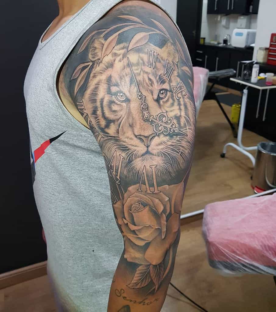 An arm tattoo featuring a majestic tiger, its fierce gaze harmonizing with a clock adorned in Roman numerals, and complemented by an elegant rose design