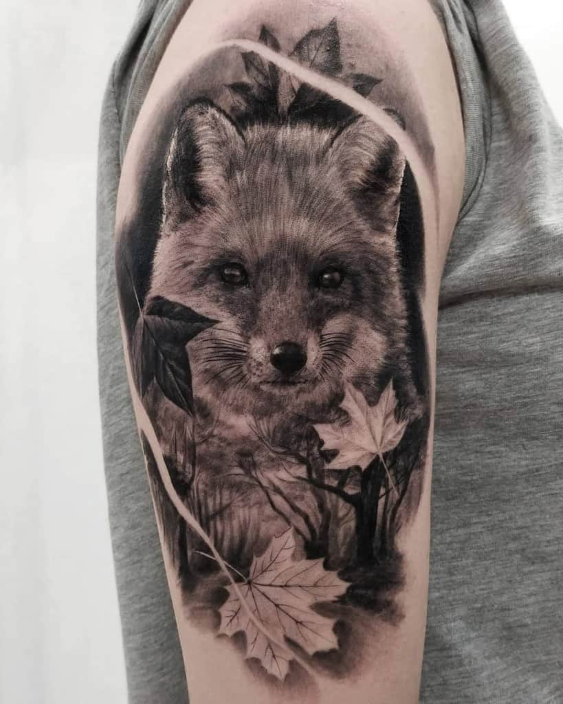 Black and white tattoo of a fox with leaves on an upper arm