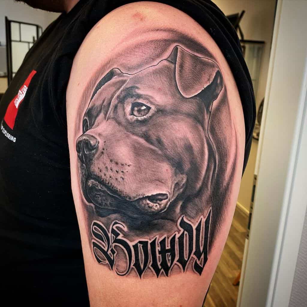 A detailed tattoo of a dog's face with the word "Howdy" on an upper arm