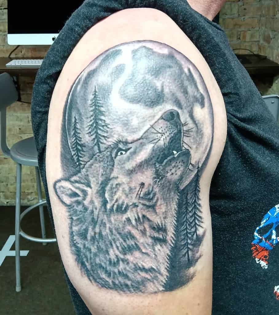 Tattoo of a wolf howling at the moon with trees in the background on an upper arm