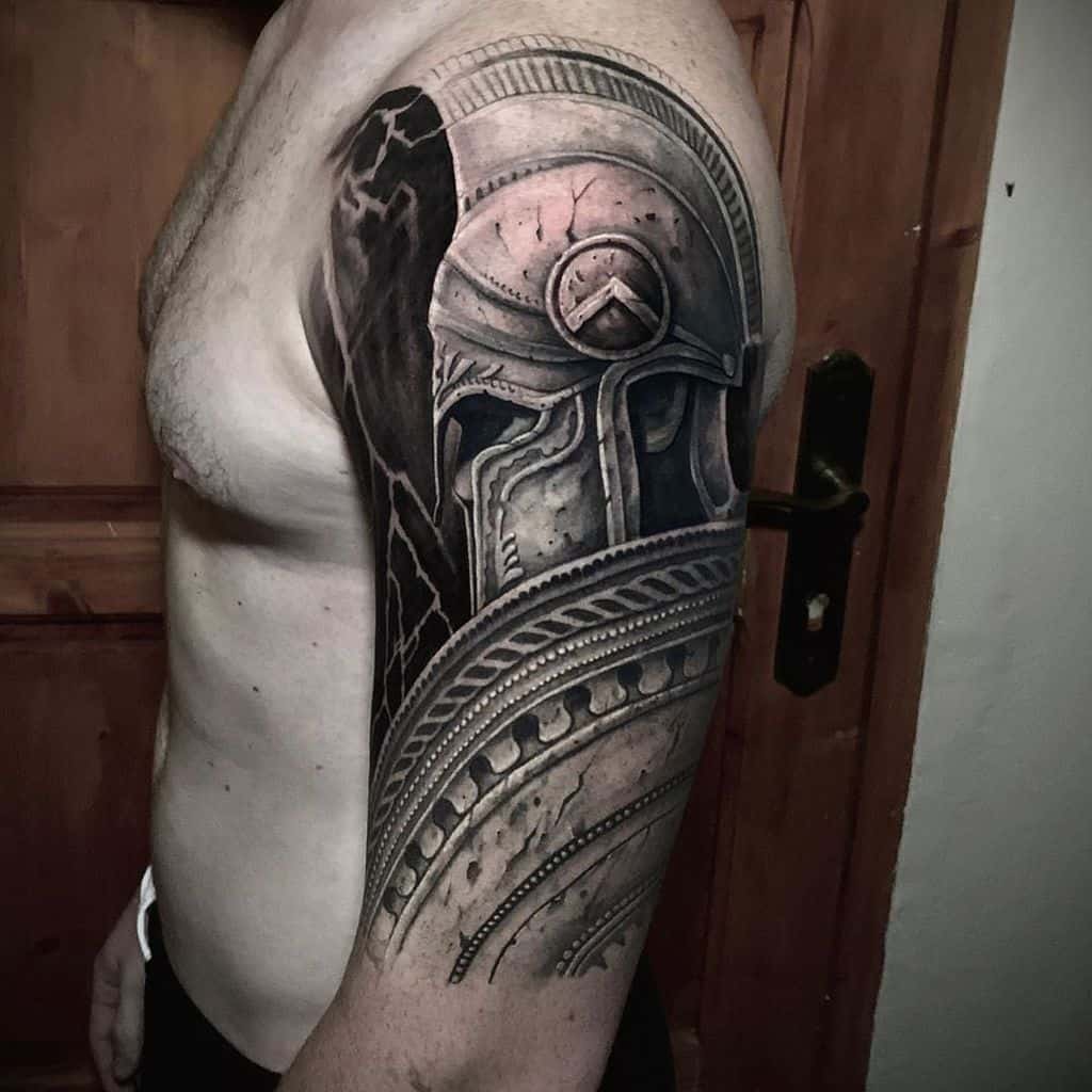 Arm tattoo depicting a detailed Spartan warrior helmet, covering the shoulder and upper arm