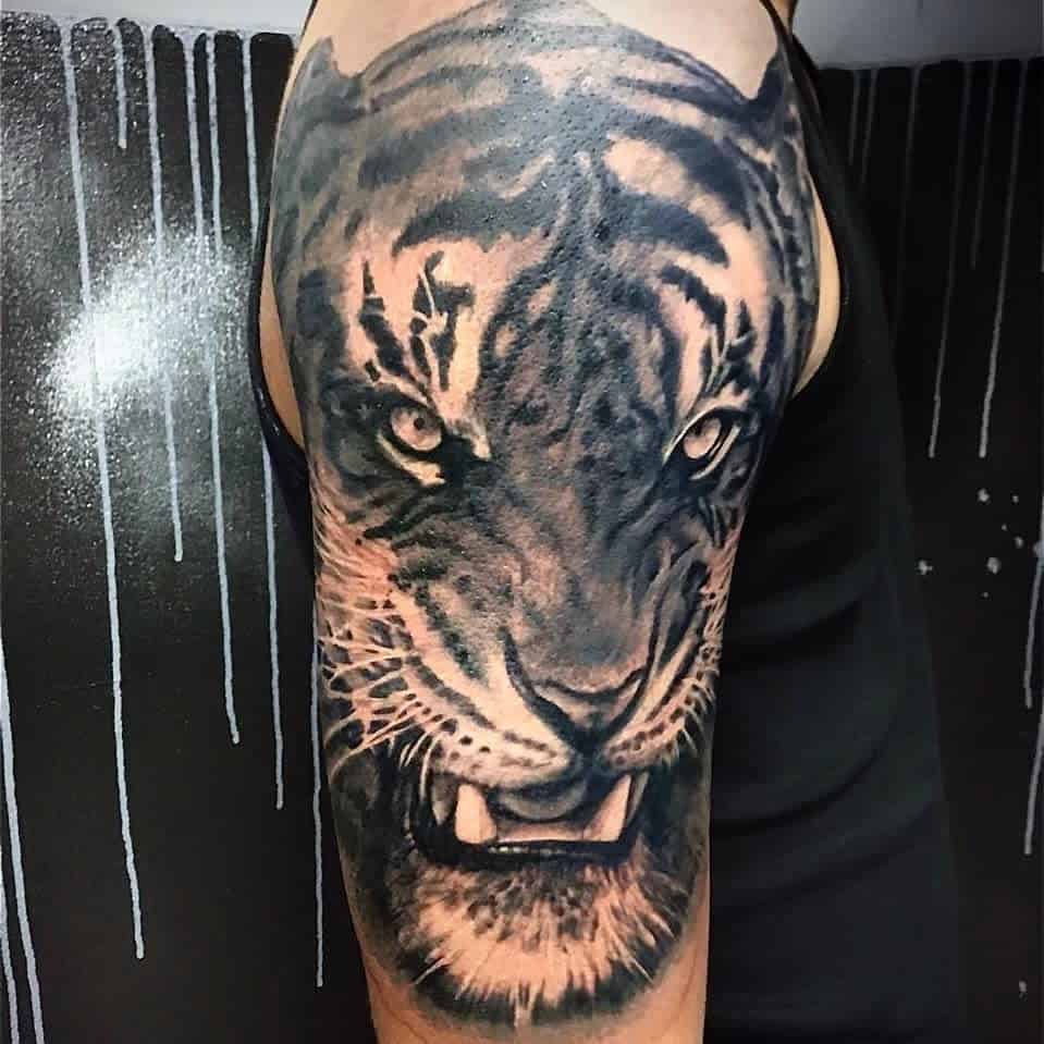 Tiger face tattoo on upper arm against a dark, drippy textured background