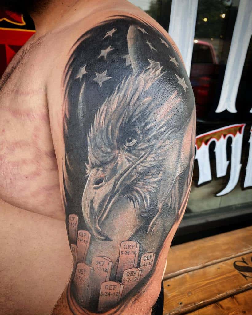 Realistic upper arm tattoo featuring a fierce eagle with an American flag and military gravestones, symbolizing patriotism and remembrance