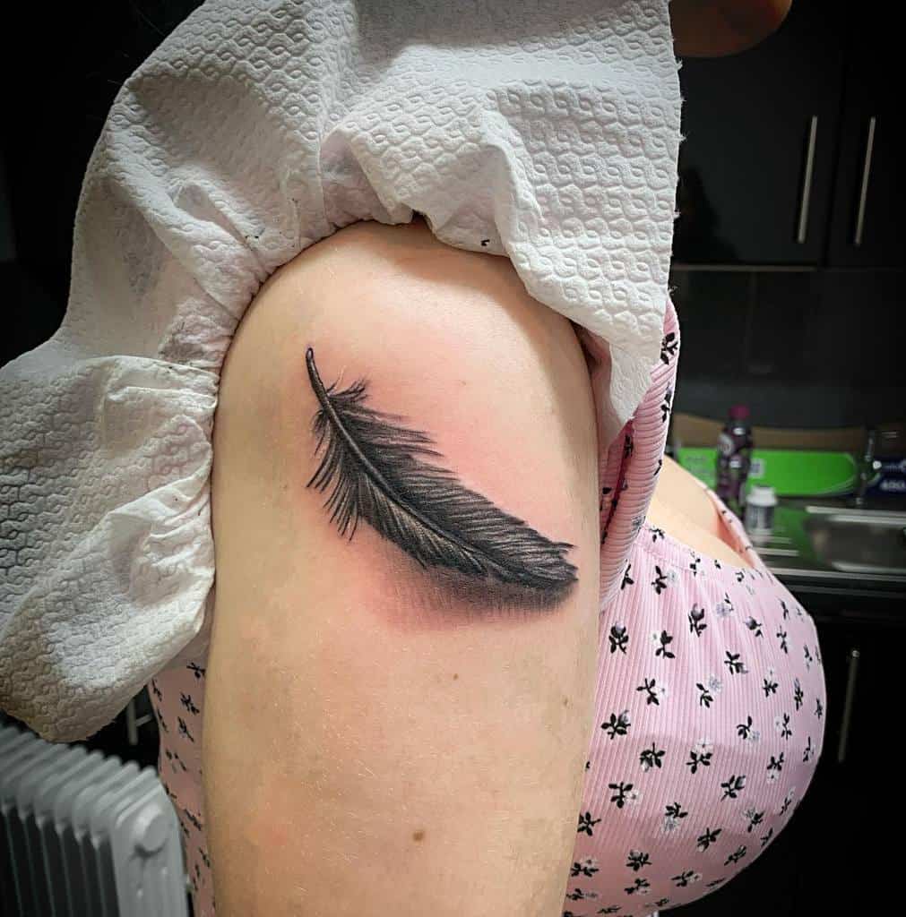 A black feather tattoo on an upper arm