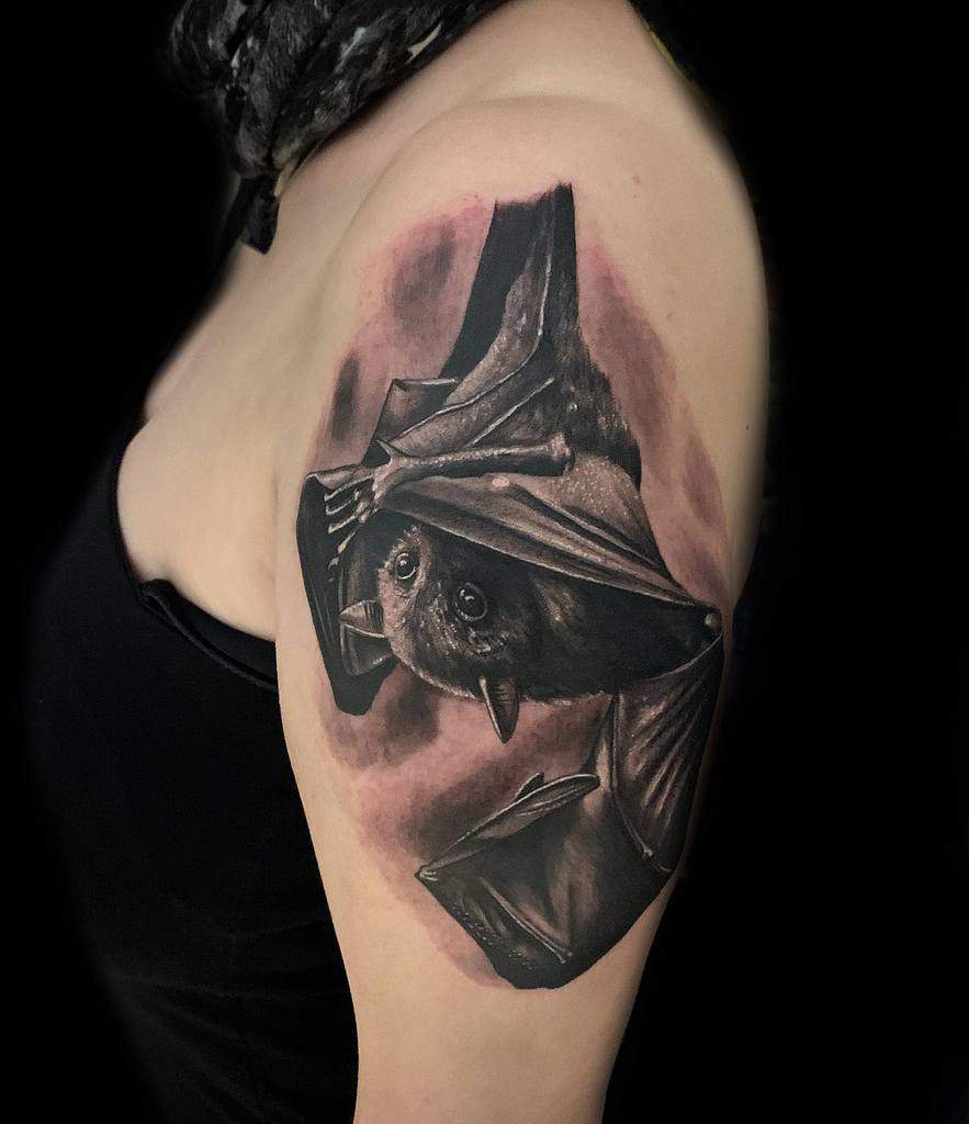 Realistic tattoo of a bat hanging upside down on a woman's upper arm
