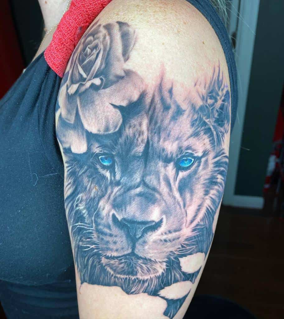 A lion and rose tattoo on a woman's upper arm, with vibrant blue eyes and intricate shading